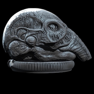 May include: A grey, sculpted object with an elongated, organic, and biomechanical form featuring intricate, vein-like textures and recessed cavities. The sculpture rests upon a circular, ribbed base with a consistent, uniform grey finish.