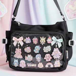 Peut inclure: Un sac bandoulière noir doté d'une poche frontale transparente remplie de diverses épinglettes et breloques de personnages colorés. Le sac comprend une sangle noire réglable, des poches latérales avec boucles blanches et deux nœuds décoratifs.