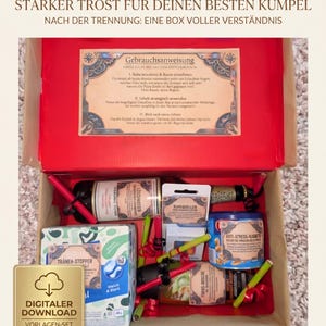 Könnte beinhalten: Eine rote Box gefüllt mit Artikeln, darunter eine Weinflasche, Snacks und Taschentücher. Die Box enthält deutschen Text, darunter "Starker Trost für deinen besten Kumpel" und "Digitaler Download Vorlagen-Set".
