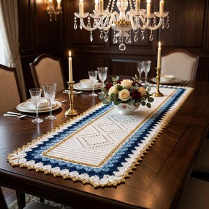 Könnte beinhalten: Ein rechteckiger Häkel-Tischläufer mit weißer Mitte und Rautenmuster, umrandet von blauen und goldenen Garnschichten. Der Läufer liegt auf einem dunklen Holztisch unter einem Blumenarrangement in einer weißen Schale.