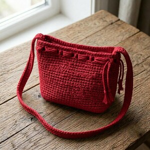 Può includere: Una borsa a tracolla all'uncinetto di colore rosso vivace, caratterizzata da un corpo rettangolare strutturato con un motivo a punti denso e testurizzato. La borsa include una tracolla all'uncinetto abbinata e una chiusura a coulisse.