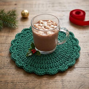 May include: A clear glass mug filled with hot chocolate topped with white marshmallows sits on a round, dark green crocheted coaster. A small sprig of green holly leaves with three red berries rests on the coaster next to the glass mug.