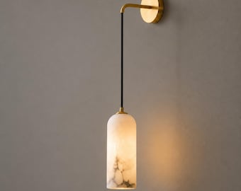 May include: A wall-mounted light fixture featuring a circular brass wall plate, a thin black vertical rod, and a cylindrical white marble shade with grey veining. The light emits a warm glow from the bottom of the stone-textured pendant.