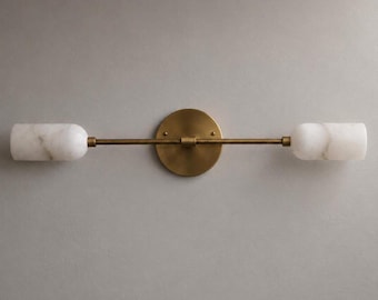 May include: A horizontal wall light fixture featuring a circular brass backplate and a thin central rod extending to two cylindrical white marble shades. The metal components have a brushed brass finish, while the stone shades display natural veining.