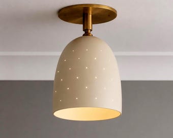 May include: A flush mount ceiling light fixture featuring a dome-shaped off-white shade with small perforated holes that allow light to pass through. The shade is attached to a circular brass-toned metal canopy by a short, cylindrical stem.