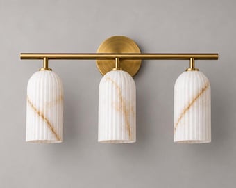 May include: A three-light wall fixture featuring a horizontal brass bar and a circular brass wall mount. Three cylindrical, vertically ribbed white glass shades with gold-toned veining hang from the bar, creating a balanced lighting design.