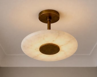 May include: A flush mount ceiling light fixture featuring a circular, translucent white stone shade with subtle veining. The fixture includes a central brass-toned metal disc and a matching cylindrical stem connecting to a circular ceiling canopy.