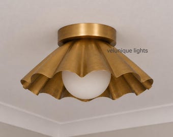 May include: A flush mount ceiling light fixture featuring a wide, scalloped brass shade with a brushed metallic finish. A single spherical white glass globe bulb is centered within the shade. The text velunique lights is visible on the shade.