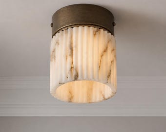 May include: A flush mount ceiling light fixture featuring a cylindrical, vertically fluted white shade with brown marble-like veining. The shade is secured by a circular, dark bronze-toned metal base that attaches directly to the ceiling surface.