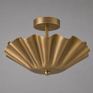May include: A flush mount ceiling light fixture with a wide, scalloped, bowl-shaped shade in a brushed brass finish. The fixture features a central stem connecting the shade to a circular canopy and a small, rounded finial at the bottom center.