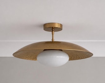 May include: A ceiling light fixture featuring a wide, shallow, brushed brass metal shade with a perforated edge. A central, smooth, opaque white glass globe sits beneath the metal disc, attached to a matching brass canopy by a short rod.