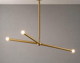 May include: A brass-finished ceiling light fixture featuring a central vertical rod connected to a horizontal bar. Three slender arms extend from a central sphere, each tipped with a small, glowing white spherical light bulb, creating a linear design.