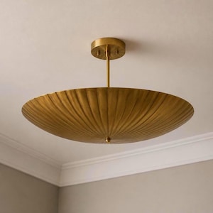 May include: A brass ceiling light fixture featuring a wide, shallow, bowl-shaped shade with a distinct radial fluted texture. The fixture is suspended by a central vertical rod attached to a circular canopy mounted flush against the ceiling.