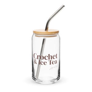 Könnte beinhalten: Ein durchsichtiges Glas mit einem Bambusdeckel und einem gebogenen Metallstrohhalm. Auf der Vorderseite des Glases ist der dunkelbraune Schriftzug Crochet & Ice Tea aufgedruckt, darunter steht in kleinerer Schreibschrift joy of life.