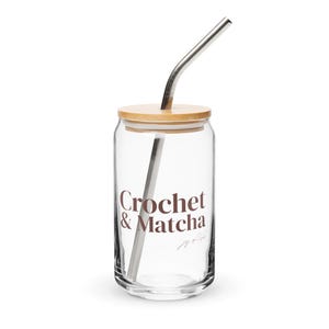 Könnte beinhalten: Ein durchsichtiges Glas mit Bambusdeckel und einem gebogenen Metallstrohhalm. Auf der Vorderseite ist der braune Schriftzug "Crochet & Matcha" sowie der kleinere kursive Text "joy of life" aufgedruckt. Das Glas ist zylindrisch mit abgerundetem Boden.