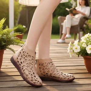 Puede incluir: Un par de botines de color beige con un patrón geométrico cortado a láser en la parte superior, un borde festoneado, cierre de cremallera en la parte posterior y una suela plana de color marrón oscuro. El diseño presenta aberturas.