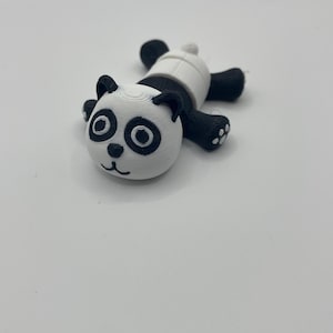 Peut inclure: Une clé USB en forme de panda imprimée en 3D, dotée d'une tête blanche avec des taches oculaires, des oreilles et un nez noirs. Le corps est blanc avec des membres noirs et une petite queue blanche. Les couches d'impression sont visibles.