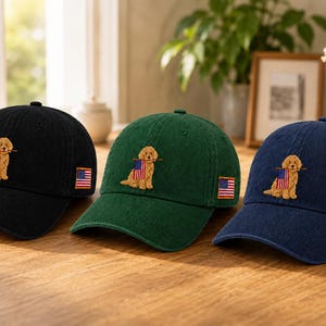 May include: Three baseball caps in black, dark green, and navy blue. Each cap features an embroidered golden-brown dog holding a small American flag in its mouth on the front, and a small American flag patch on the side of the cap.