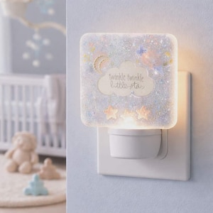 May include: A square night light with a glittery, starry design. The night light has the words "twinkle twinkle little star" on it. The night light is plugged into a white wall outlet.