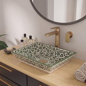 May include: A rectangular ceramic vessel sink featuring a dark green floral pattern on a white background, paired with a brushed gold faucet and wall-mounted handle. The sink sits on a light wood countertop above a dark cabinet with gold hardware.