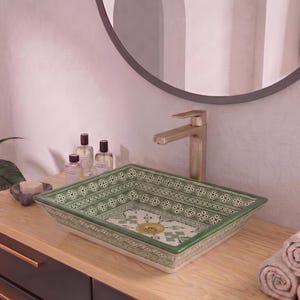 May include: A rectangular ceramic vessel sink featuring a green and white geometric pattern on the interior and exterior walls. The sink includes a gold-toned drain and is paired with a tall, brushed gold faucet mounted on a light wood vanity top.