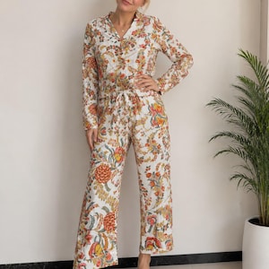 Könnte beinhalten: Ein zweiteiliger Schlafanzug bestehend aus einem langärmeligen Hemd mit Knopfleiste und Reverskragen sowie einer passenden Hose mit geradem Bein. Das Set besteht aus weißem Stoff mit einem floralen Muster in Orange, Gelb und Grün.