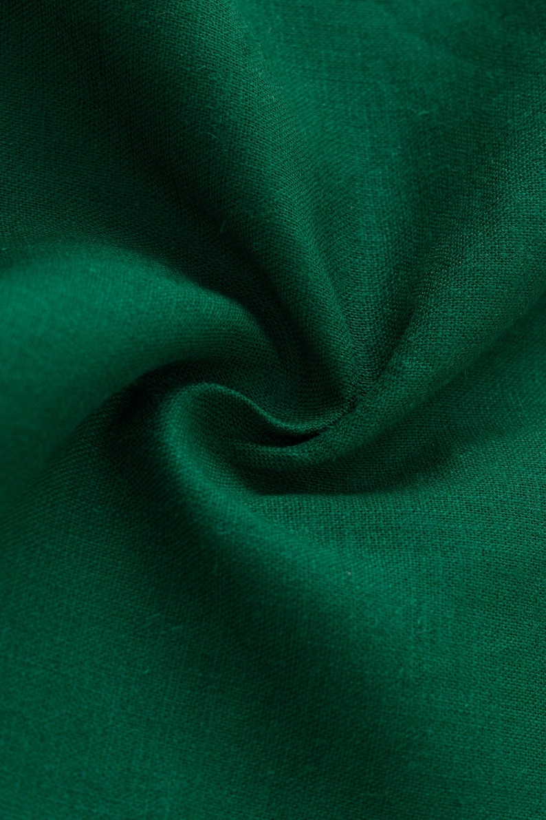 May include: A deep forest green fabric with a visible woven texture. The material is gathered in the center, creating soft, flowing folds and shadows that highlight the consistent, solid color and the natural weave of the textile surface.