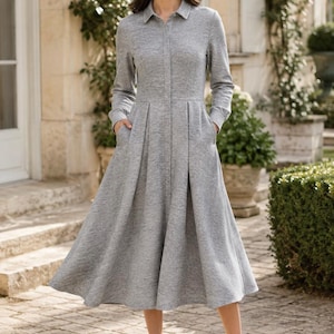May include: A heather grey midi-length shirt dress featuring a collared neckline, long sleeves, a button-down front placket, and a fitted bodice that transitions into a pleated, flared skirt with side pockets, crafted from a soft jersey fabric.