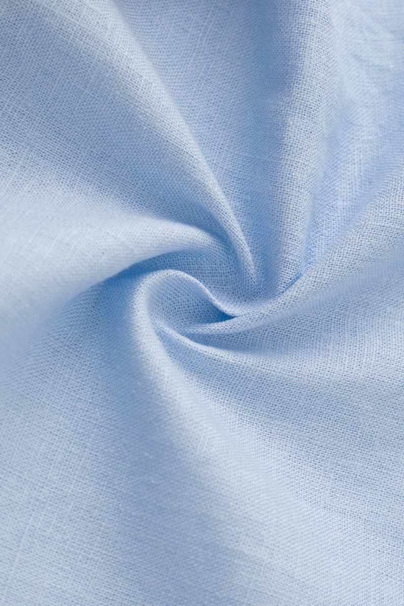 May include: A light blue fabric with a visible woven texture and a soft, matte finish. The material is gathered in the center, creating natural folds and shadows that highlight the consistent weave pattern and the solid, pale blue color throughout.