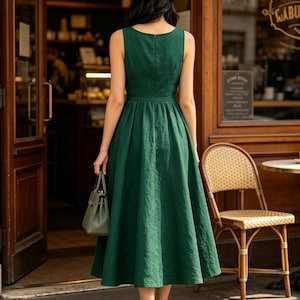 May include: A sleeveless forest green midi dress with a fitted bodice and a flared, pleated skirt. The dress features a round neckline and a concealed back zipper closure. A small, matching green structured handbag is held at the side.