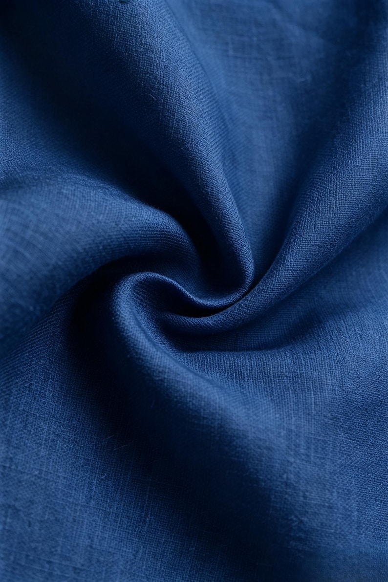 May include: A deep blue fabric with a visible woven texture and a natural fiber appearance. The material is gathered into soft, flowing folds that create subtle shadows and highlights across the surface, emphasizing the rich, solid color.