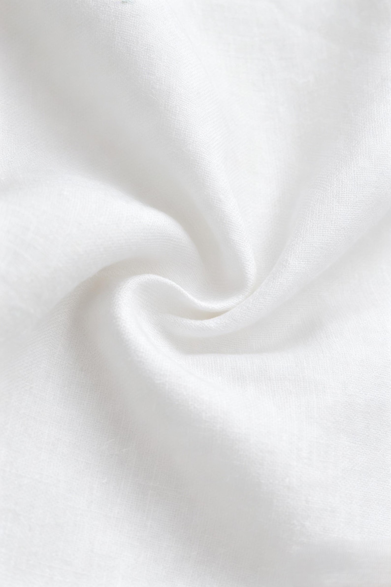 May include: A solid white fabric with a visible woven texture, featuring a central swirl or spiral fold that creates soft, natural shadows and highlights across the surface, emphasizing the material's light, breathable, and slightly translucent quality.