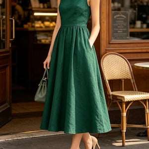 May include: A sleeveless forest green midi dress with a fitted bodice, a defined waistline, and a full, pleated skirt featuring side pockets. The dress is paired with beige high-heeled pumps and a small, matching green structured handbag.