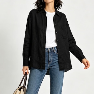 May include: A black long-sleeved button-down shirt worn over a plain white t-shirt and blue denim jeans. The black shirt features a classic collar, a single chest pocket, and dark buttons running down the front placket and on the sleeve cuffs.