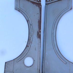 May include: Two symmetrical, unfinished gray metal automotive fender panels featuring curved wheel arch cutouts. The left panel includes a circular opening near the bottom. Both pieces show signs of surface wear and oxidation along the edges.