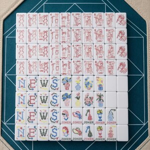 Op de afbeelding: Een set witte mahjongtegels gerangschikt in een raster. De bovenste rijen bevatten rode lijntekeningen van linten en paarden, genummerd van &eacute;&eacute;n tot negen. De onderste rijen tonen het woord NEWS in blauw en zwart, bloemenvazen en JOKER-tegels.