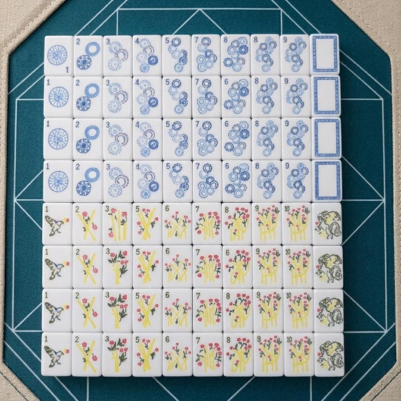 Op de afbeelding: Een set witte rechthoekige mahjongtegels gerangschikt in een raster. De bovenste vier rijen bevatten blauwe cirkelvormige en tandwielachtige patronen met de cijfers &eacute;&eacute;n tot en met negen en een lege tegel. De onderste rijen tonen kleurrijke bloem- en vogelillustraties.