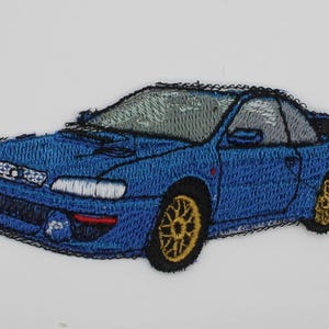 May include: An embroidered patch featuring a blue sports car with gold wheels, a rear spoiler, and grey windows. The design is rendered in blue, gold, grey, and black thread, capturing the vehicle's front-facing angle and detailed body lines.
