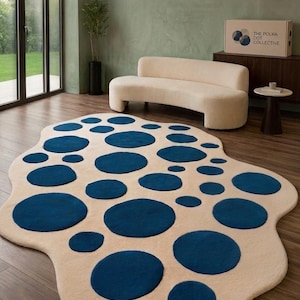 May include: An irregular, organic-shaped area rug featuring a cream-coloured base with numerous dark blue circular patterns of varying sizes scattered across the surface. The rug has a soft, textured pile and a non-symmetrical, fluid perimeter.