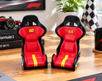 以下が含まれることがあります： 黒と赤のミニチュアレーシングバケットシート2脚。左のシートには黄色の数字16、右のシートには黄色の数字44が記されています。両方のシートの座面中央には黄色のストライプが入っています。
