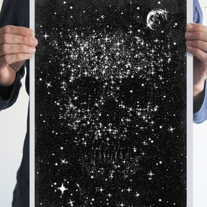 May include: Black and white art print depicting a starry night sky with a crescent moon. The artwork features a dense cluster of stars and a scattering of smaller stars against a dark background. The print is held by a person.