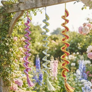 Peut inclure: Trois décorations en spirale suspendues en fil crocheté. La spirale de gauche est rose et blanche, celle du milieu est bleu clair et jaune, et celle de droite est jaune et rouge. Chaque spirale possède un pompon en fil assorti à la base.