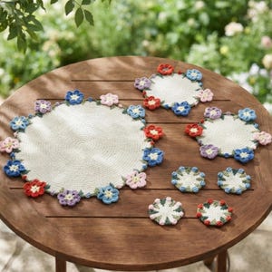 Peut inclure: Un ensemble de sets de table et dessous de verre circulaires au crochet de tailles variées, avec un centre blanc cassé au motif texturé. Chaque pièce est bordée de petites fleurs crochetées en relief dans des tons de rouge, bleu et rose.