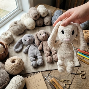 Peut inclure: Poupées lapin au crochet faites à la main en crème, gris et marron. Les lapins ont de longues oreilles, un nez rose et des yeux noirs. Des pelotes de laine de différentes couleurs neutres et des crochets sont disposés autour des poupées.