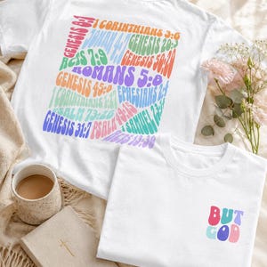 Puede incluir: Una camiseta blanca con un gráfico grande y colorido en la parte posterior que presenta varias referencias de versículos bíblicos en una fuente ondulada de estilo retro. El frente de la camiseta muestra el texto "BUT GOD" en una fuente retro.