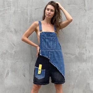 Könnte beinhalten: Jeans-Latzhose im zweifarbigen Design mit einem hellblauen Oberteil und einem dunkelgrauen Unterteil. Das Kleidungsstück verfügt über einen asymmetrischen Saum, eine Brusttasche und eine dunkle Beintasche, die mit einem leuchtend gelben Riemen akzentuiert ist.