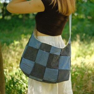 Puede incluir: Un bolso de hombro estilo hobo confeccionado con un mosaico de cuadrados de tela vaquera en tonos alternos de azul claro y gris carb&oacute;n oscuro. El bolso cuenta con una correa de hombro ancha integrada y una silueta holgada y desestructurada.