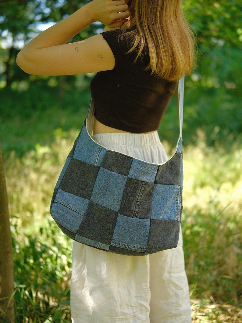 Puede incluir: Un bolso de hombro estilo hobo confeccionado con un mosaico de cuadrados de tela vaquera en tonos alternos de azul claro y gris carb&oacute;n oscuro. El bolso cuenta con una correa de hombro ancha integrada y una silueta holgada y desestructurada.