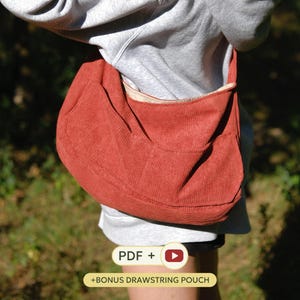 May include: A rust-coloured corduroy hobo bag with a wide shoulder strap and a curved silhouette. The bag features a visible exterior pocket and a light-coloured interior lining. Text on the image reads: PDF + [play icon] + BONUS DRAWSTRING POUCH.