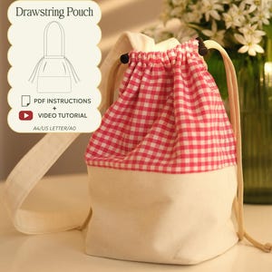 Può includere: Una sacca con coulisse caratterizzata da una sezione superiore a quadretti vichy rosa e bianchi e una sezione inferiore in tela color crema. La borsa include cordini beige e fermi neri. Un riquadro mostra il testo Drawstring Pouch, PDF INSTRUCTIONS, VIDEO TUTORIAL, A4/US LETTER/A0, NO AI.